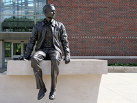 Photo of a statue of Neil Armstrong sitting on a ledge. The words