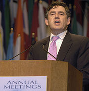 Gordon Brown standing at a podium. Text on the podium states
